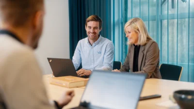 tre personer sitter vid ett bord med datorer